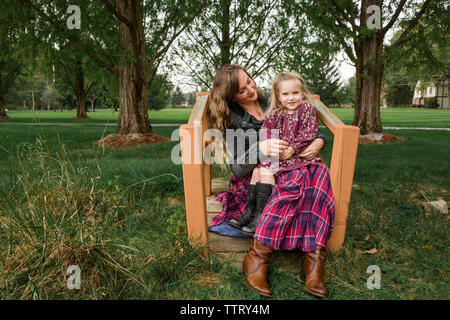 Portrait of daughter sitting on mother's lap at park Stock Photo