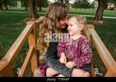 Close-up of daughter sitting on mother's lap at park Stock Photo