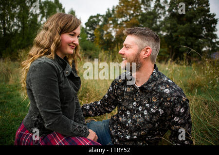Happy couple sitting on grassy field at farm Stock Photo