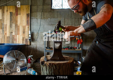 Blacksmith hammering knife on anvil in workshop Stock Photo