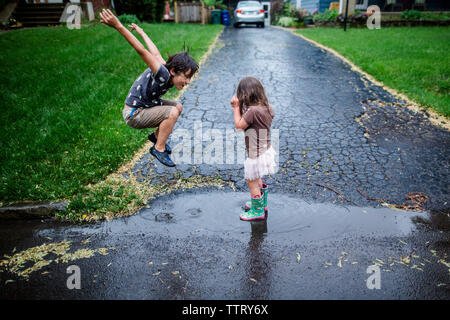 Side view of playful siblings enjoying on wet road during rainy season Stock Photo