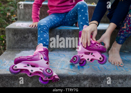 Low section of mother assisting daughter in wearing roller skates while sitting on steps Stock Photo