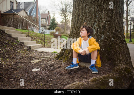 Thoughtful boy looking away while sitting by tree trunk Stock Photo