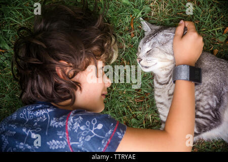 High angle view of boy petting cat while lying on grassy field in yard Stock Photo