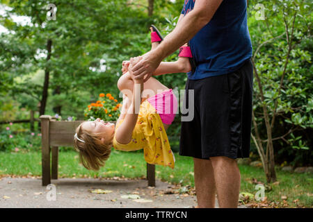 Midsection of playful father carrying cute daughter while standing against trees in yard Stock Photo