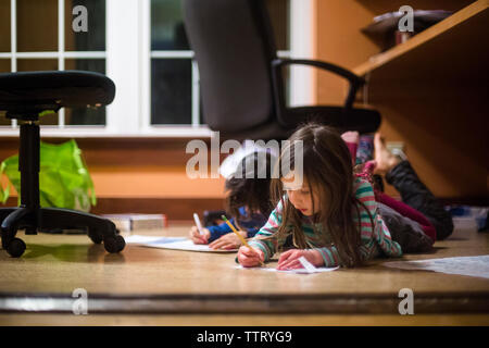 Siblings lay down on the floor together doing their homework Stock Photo