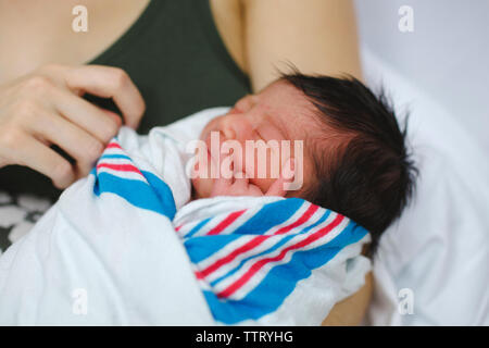 a newborn girl wrapped in a blanket, rests in her mother's arms Stock Photo