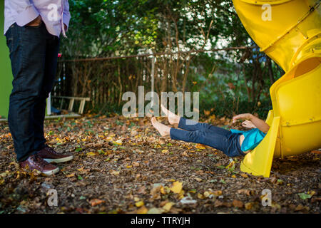 the bottom half of a child emerges from a slide as her father watches Stock Photo