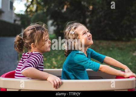 two cute little girls sit happily together in a wagon Stock Photo