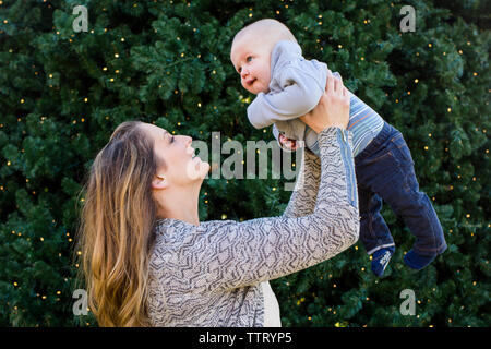 A smiling mother tenderly lifts her baby boy into the air Stock Photo