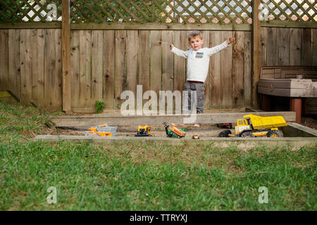 a barefoot little boy plays with trucks in a sand pit Stock Photo