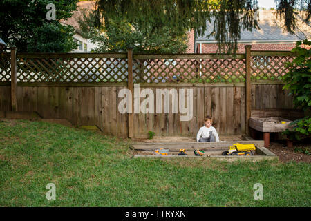 a small boy plays in a sandbox in yard Stock Photo