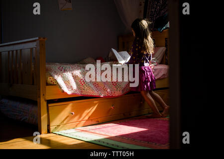 rear view of a small girl reading a book alone in her bedroom Stock Photo