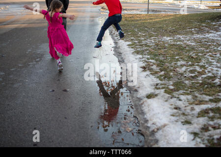 Two happy children leap and dance on walk down the street with father Stock Photo