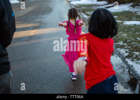 two small children march happily down snowy street with their parent Stock Photo