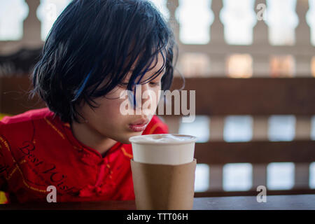 top half of a boy blowing on a cup of hot chocolate in an outdoor cafe Stock Photo