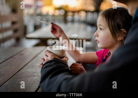 A young child sits with her father at an outdoor cafe at sunset Stock Photo