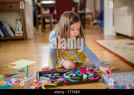 A little girl peacefully sits on living room floor with an art project Stock Photo