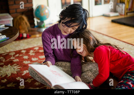 Two small children cuddle together on the living room floor reading Stock Photo