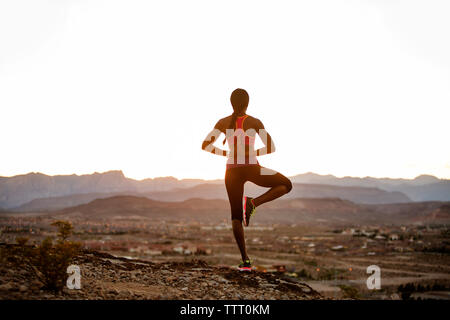 Rear view of woman practicing yoga on landscape against clear sky Stock Photo