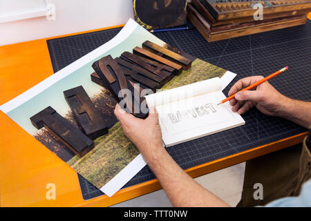Cropped image of man holding wooden alphabets and copying in paper Stock Photo