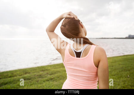 Rear view of woman stretching on grassy field against sky on sunny day Stock Photo