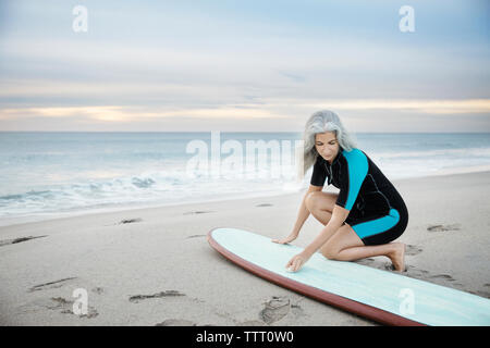 Female surfer cleaning surfboard at Delray beach during sunset Stock Photo
