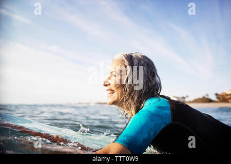 Side view of happy mature woman lying on surfboard in sea Stock Photo