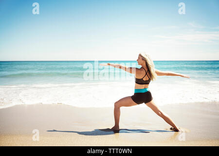 Rear view of determined woman practicing yoga in Warrior 2 pose on Delray beach Stock Photo