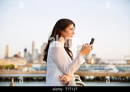 Side view of woman holding smart phone while standing at