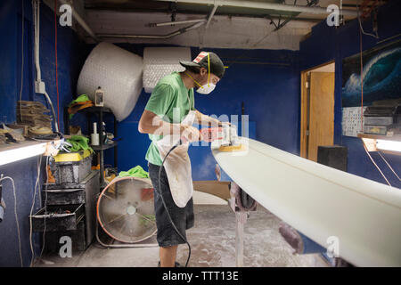 worker using sander on surfboard in workshop Stock Photo
