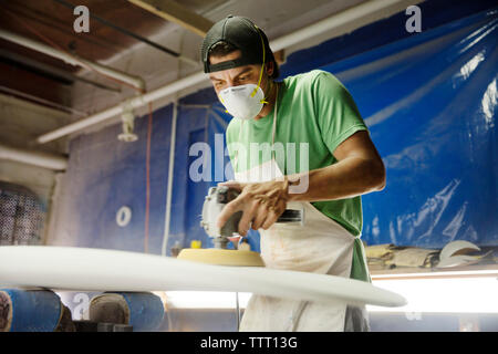 worker using sander machine on surfboard in workshop Stock Photo