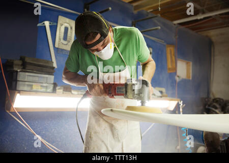 worker using sander while making surfboard in workshop Stock Photo