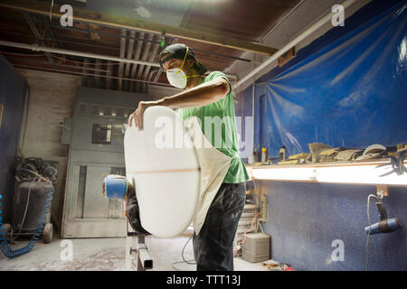 worker holding surfboard while standing in workshop Stock Photo