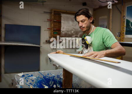 Concentrated male worker measuring surfboard in workshop Stock Photo
