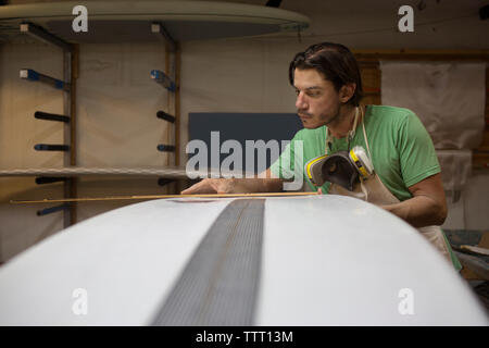 Dedicated worker measuring with ruler surfboard in workshop Stock Photo