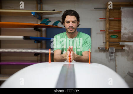 Concentrated worker adjusting fins on surfboard in workshop Stock Photo