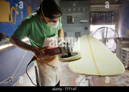 Male worker using sander on surfboard in workshop Stock Photo