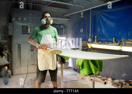 Portrait of male worker wearing protective mask while holding sander in workshop Stock Photo