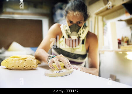 Woman using sander on surfboard in workshop Stock Photo