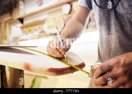 Midsection of man measuring surfboard at workshop Stock Photo