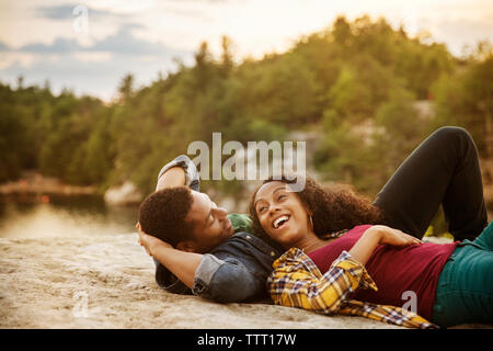 Happy couple lying on rock at lakeshore Stock Photo