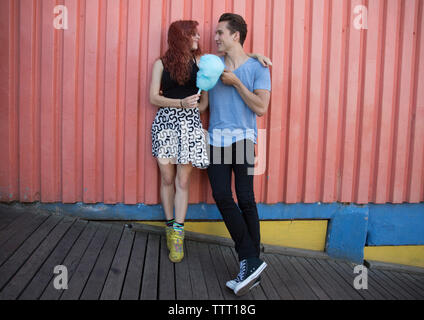 Young couple holding cotton candy while standing against wall Stock Photo