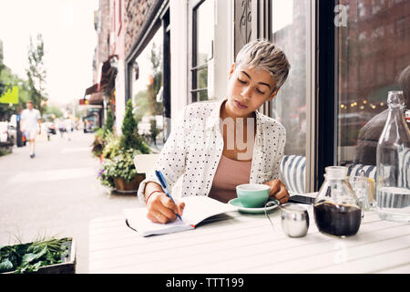 Woman writing in diary at sidewalk cafe Stock Photo