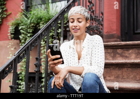 Happy woman using mobile phone while sitting on steps Stock Photo