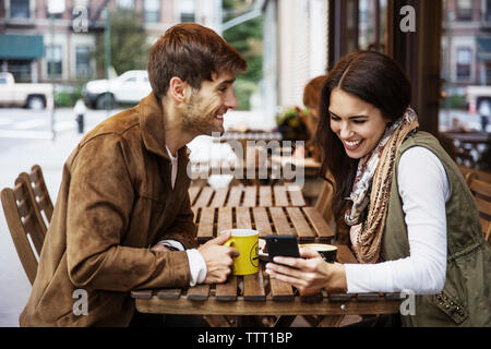 Man looking at girlfriend using mobile phone at cafe Stock Photo