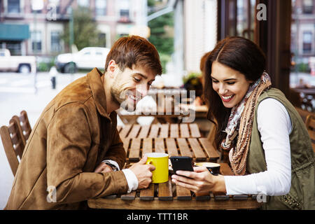 Happy couple looking at mobile phone while enjoying drinks at cafe Stock Photo