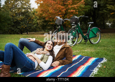 Happy couple looking at each other while relaxing on blanket in park Stock Photo