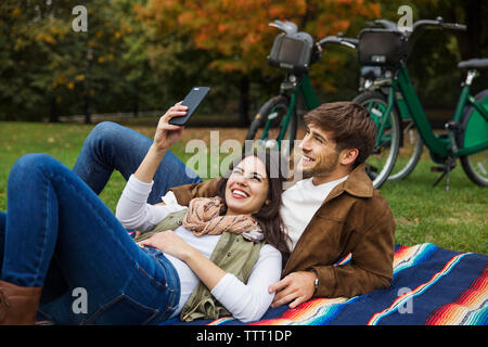 Couple taking selfie while relaxing on blanket at park Stock Photo