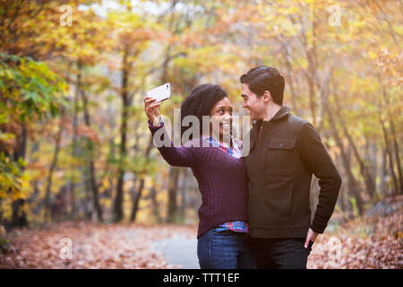 Happy couple looking at each other while taking selfie in forest Stock Photo